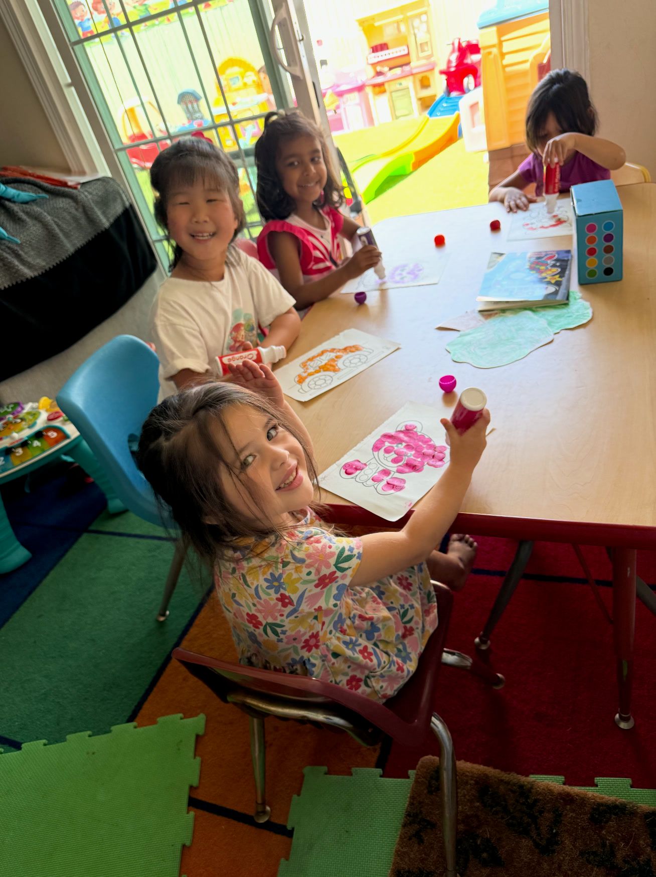Three smiling girls painting and gluing at a table
