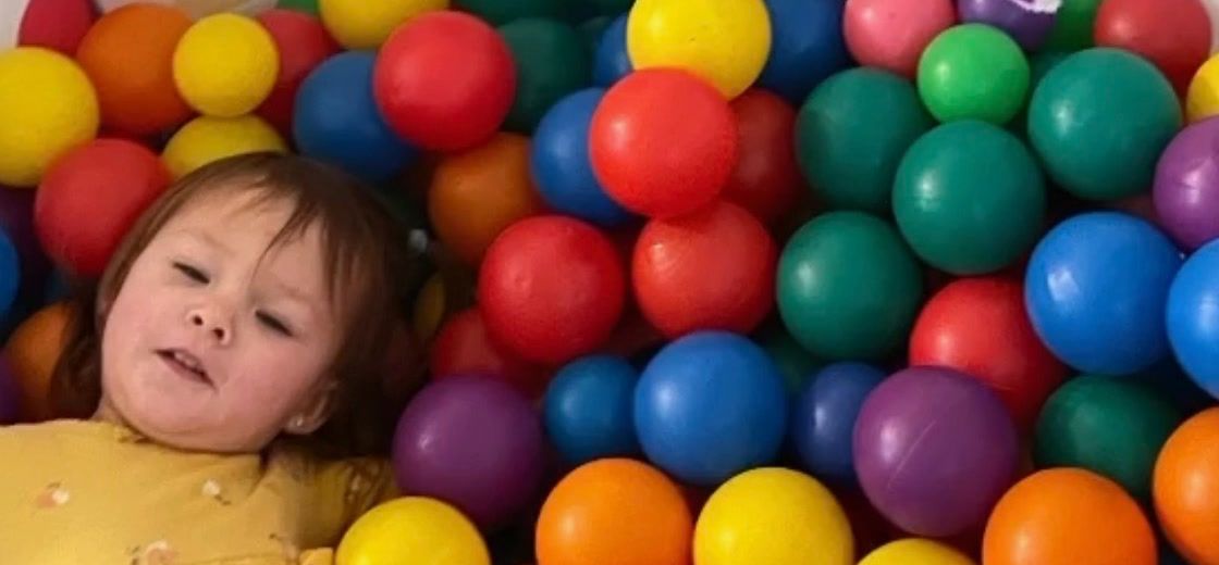 A toddler lying in a ball pit full of colorful balls
