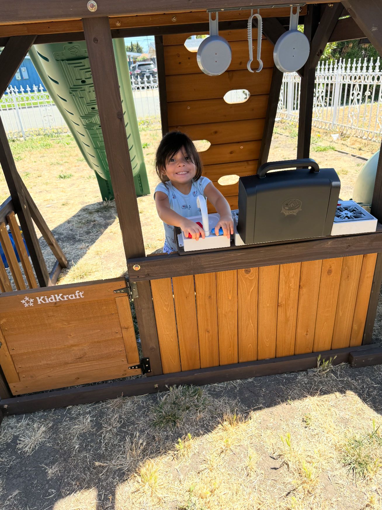 A little girl cooking pretend food in a wooden outdoor play kitchen