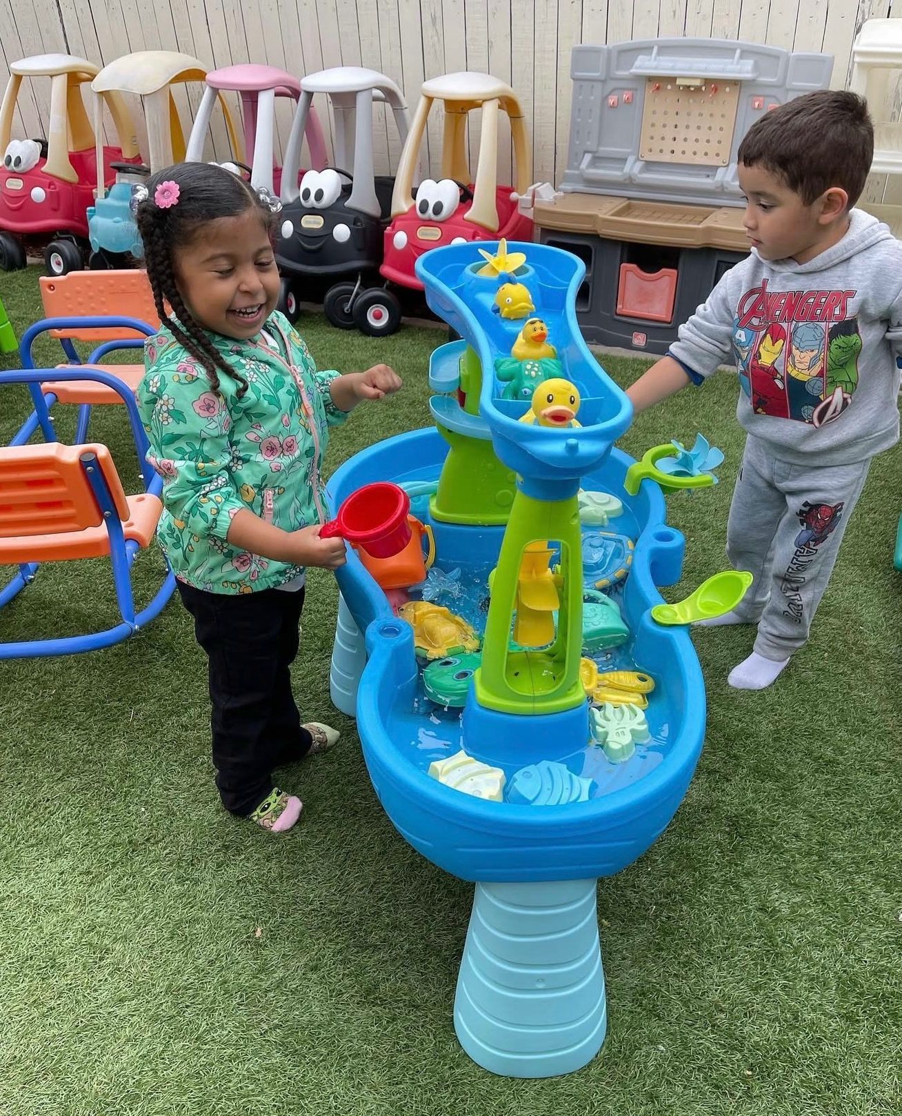 A girl and a boy playing at a blue water table with rubber ducks