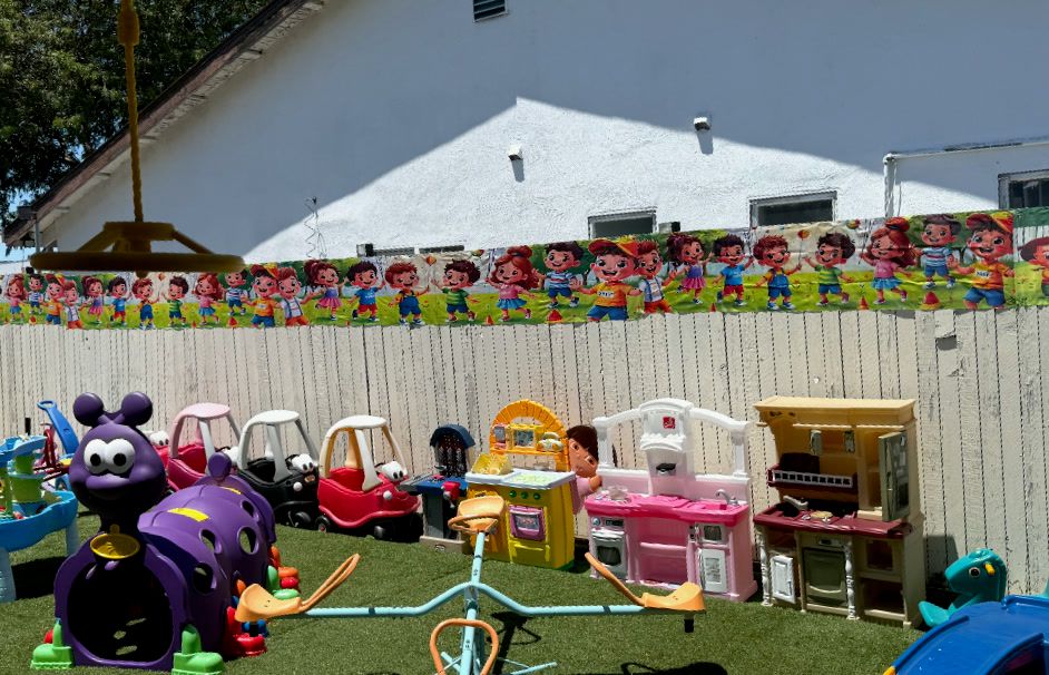 A turf play area with ride-on cars, play kitchens, a seesaw and a slide